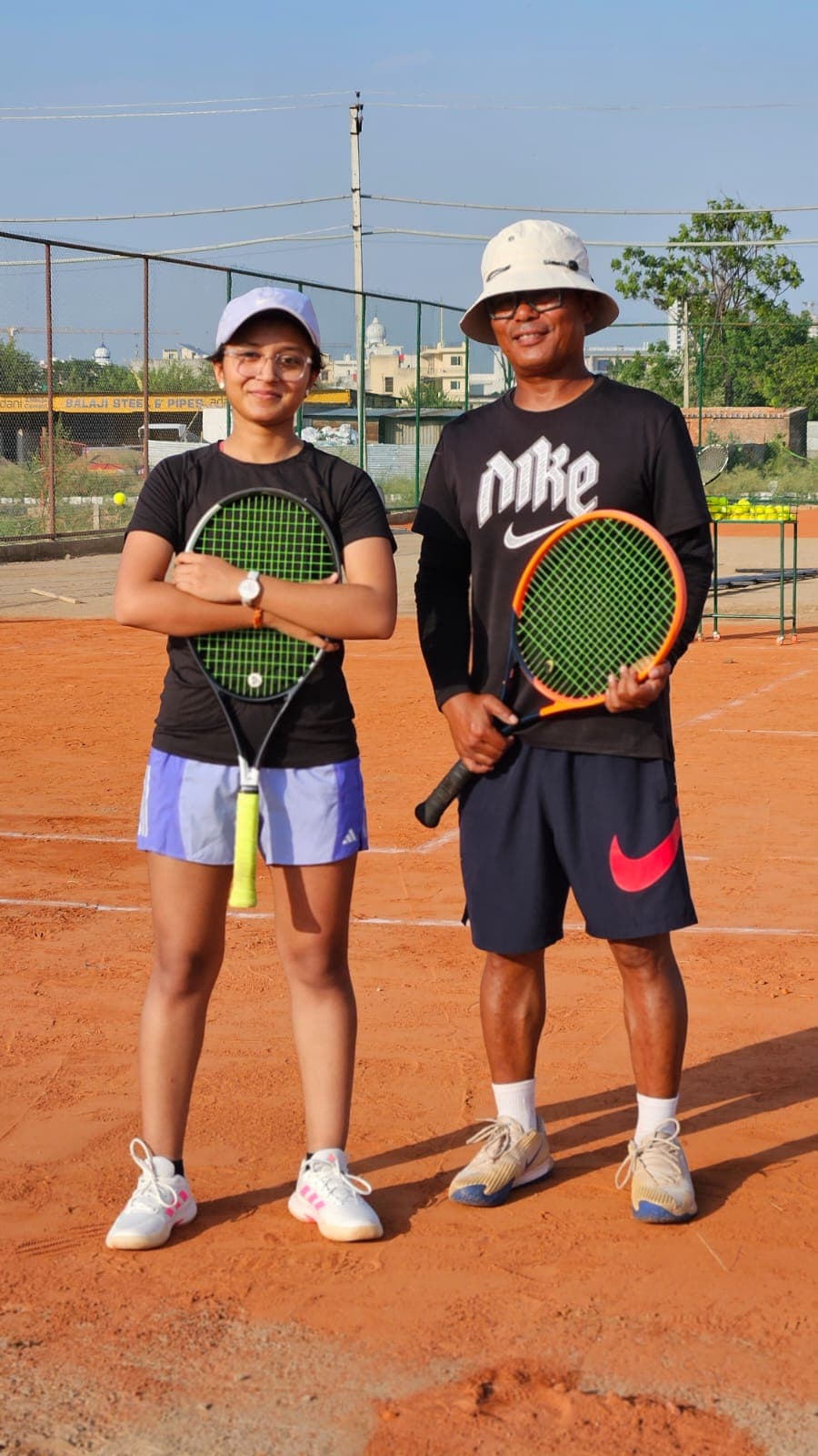 Coach and student posing with rackets on the clay court