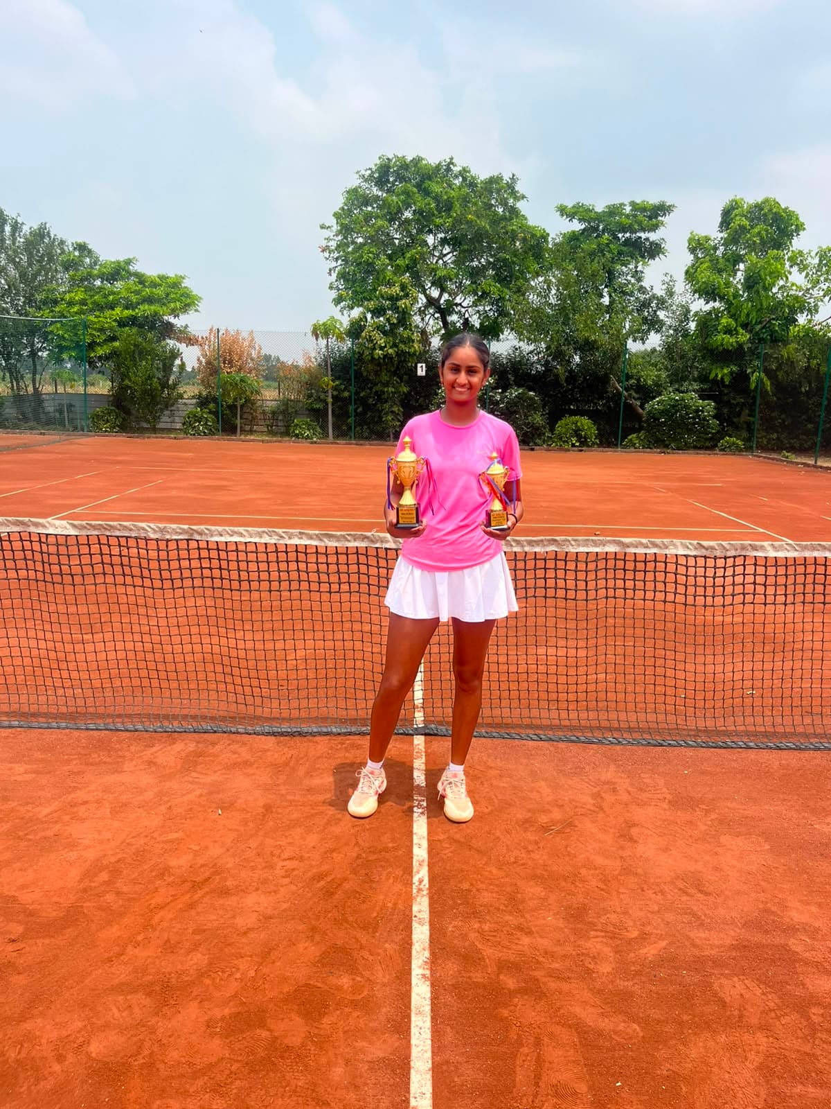 Player holding trophies at the net on clay court